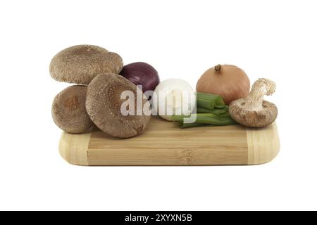 Funghi shiitake freschi, cipolle varie su un tagliere di legno isolato su sfondo bianco. Ricette di funghi ed erbe medicinali Foto Stock