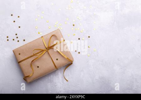 Confezione regalo avvolto in carta artigianale con nastro color oro e stelle sulla pietra grigia sullo sfondo Foto Stock