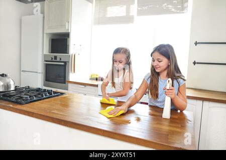 Due sorelline felici che puliscono il tavolo della cucina aiutando la madre Foto Stock