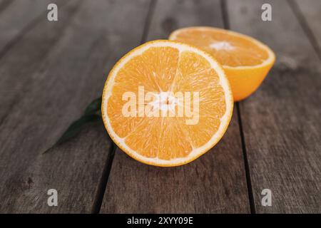 Posa piatta con metà di frutta arancione a fette fresche e mature su sfondo grigio di legno. Polpa di arancia e foglie verdi. Concetto di cibo tropicale. Mangiare sano co Foto Stock