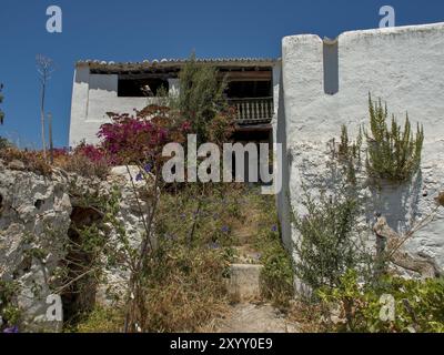 Edificio abbandonato con giardino sovrastato e piante fiorite sotto un cielo limpido, ibiza, Mar mediterraneo, spagna Foto Stock