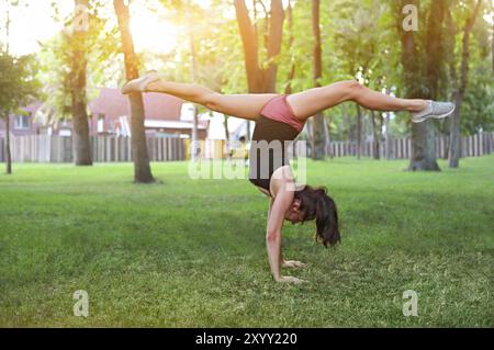 Donna che si allunga in un esercizio all'aperto sorridente felice facendo stretching dopo la corsa. Splendido modello sportivo sorridente all'aperto al tramonto d'estate Foto Stock