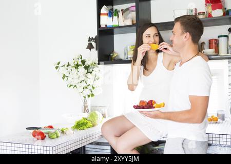 Giovane uomo e donna incinta con un piatto di frutta in kithen. La gravidanza e il concetto di nutrizione Foto Stock