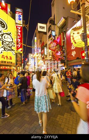 OSAKA, GIAPPONE, 23 GIUGNO 2015: Turisti che camminano intorno alla trafficata e affollata sala giochi Dotombori tra luminosi cartelli al neon e luci, il centro della vita notturna di n Foto Stock