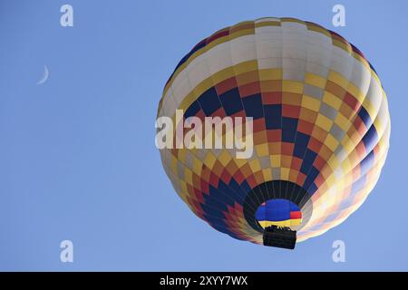 Coloratissima mongolfiera in volo e luna visto da sotto contro un cielo blu Foto Stock