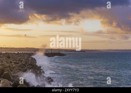 Faro di Peniche con spiaggia di Supertubos sullo sfondo al tramonto con onde che si infrangono, in Portogallo Foto Stock