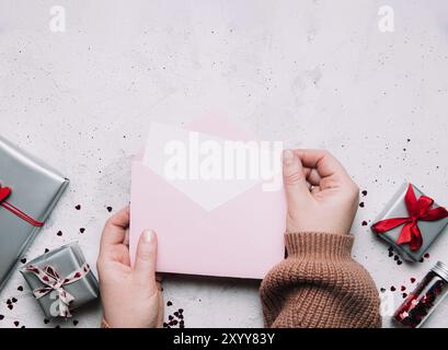 Le mani femminili tengono lettera d'amore vuoto messaggio in busta aperta, biglietto di auguri di San Valentino o invito bianco mock up. Spazio di copia, vista dall'alto. Rosa ba Foto Stock