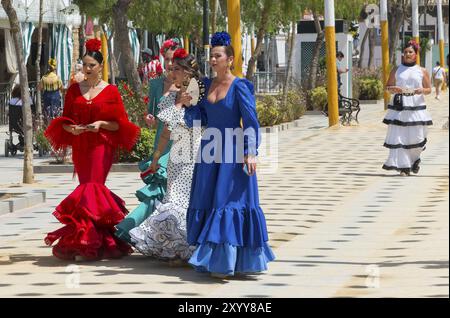 Cinque donne in diversi abiti flamenco colorati, con fiori nei capelli, passeggiando in una strada festosa, Feria de la Manzanilla, Feria de Sanluc Foto Stock