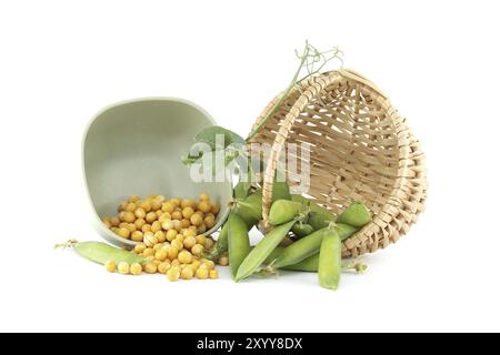 Cestello pieno di piselli verdi freschi e un recipiente riempito di piselli gialli interi secchi che fuoriescono sui lati, isolato su sfondo bianco Foto Stock