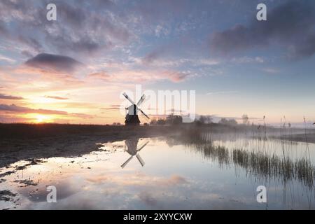 Mulino a vento sul fiume in nebbia mattutina all'alba, Paesi Bassi Foto Stock