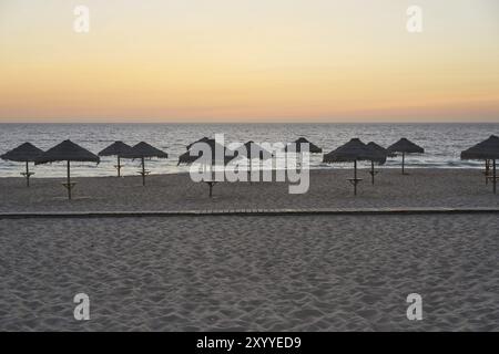 Spiaggia vuota al tramonto a Comporta, Portogallo con ombrelloni estivi di paglia Foto Stock