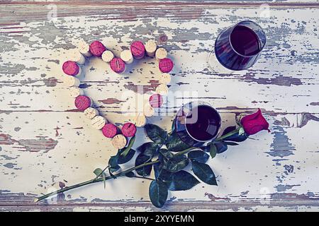 Due bicchieri di vino rosso un cuore con sughero e una rosa rossa in stile vintage Foto Stock