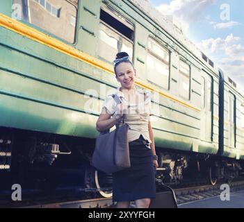 Donna con una valigia in piedi sulla piattaforma vicino alla stazione Foto Stock