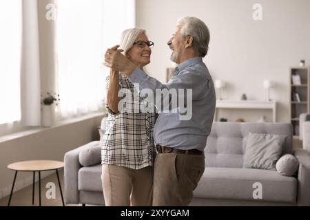 Coppia matura che si tiene per mano danzando nel salotto moderno Foto Stock