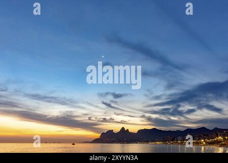 Estate tramonto a Ipanema beach in Rio de Janeiro con due fratelli hill e Gavea pietra in background e la luna nel cielo Foto Stock