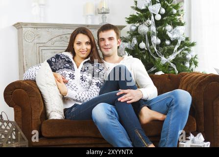 Giovane coppia felice seduto sul divano da albero di Natale Foto Stock