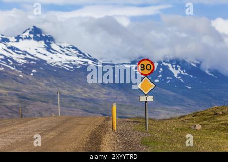 Strada di campagna con segnaletica stradale con limite di velocità e montagne innevate sullo sfondo dell'Islanda Foto Stock