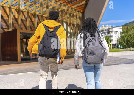 Vista posteriore di due studenti africani che camminano insieme verso l'università, tenendo i quaderni e portando con sé la borsa della scuola Foto Stock