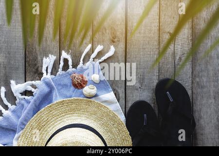 Concetto di viaggio o vacanza, fine settimana. Cappello di paglia con foglie di palma, scarpe e asciugamano, conchiglie di mare su fondo in legno. Tempo di relax. Foto Stock