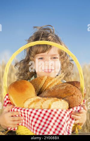 Un bambino felice che tiene in mano un cestino con pane in un campo di grano giallo autunnale sullo sfondo blu del cielo Foto Stock