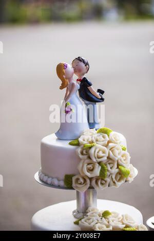 Torta nuziale con una piccola statuetta di coppia nuziale su un'etagera Foto Stock