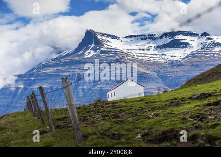 Capannone bianco con tetto rosso di fronte alle montagne innevate dell'Islanda Foto Stock