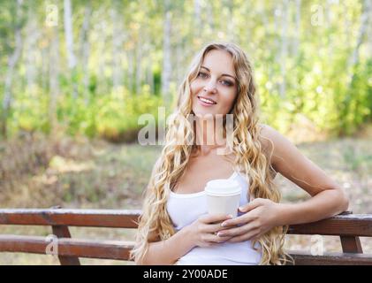 Piuttosto giovane donna bionda di bere il caffè al parco Foto Stock