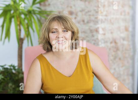 Donna matura seduti su una sedia in salotto Foto Stock