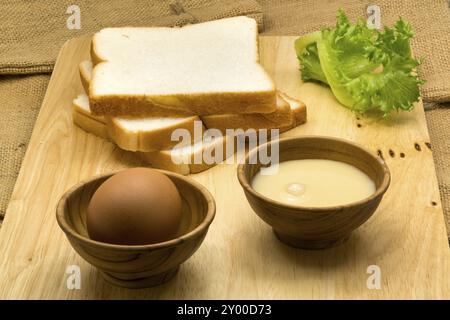 Pila di fette di pane, latte condensato zuccherato e uovo su una tavola di legno Foto Stock