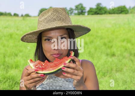 Giovanissimo colombiano donna che indossa la paglia estate hat mangiare fresco melone rosso nella natura olandese Foto Stock