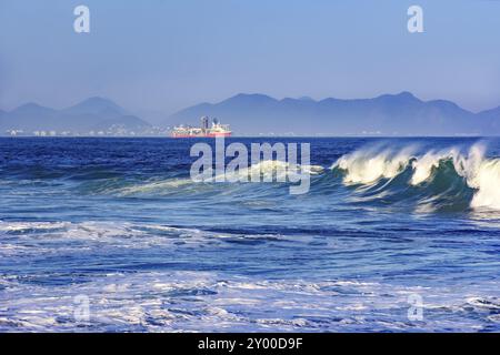 Onda sulla rottura del diavolo la spiaggia di Rio de Janeiro con la nave da carico, città e delle colline in background Foto Stock