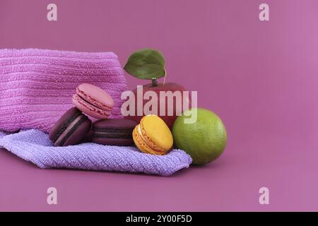 Varietà di dolci macaron a base di meringa e frutta disposti su morbidi asciugamani rosa e viola su sfondo rosa con spazio libero per il testo. DEP. Completo Foto Stock