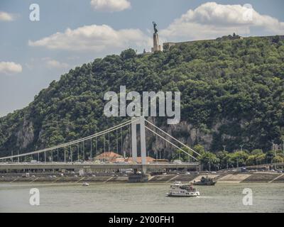 Vista di un ponte su un fiume con una collina boscosa sullo sfondo su cui si erge una statua, budapest, danubio, ungheria Foto Stock