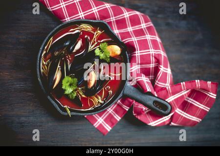 Vista dall'alto della ciotola di deliziosa zuppa con gamberi e cozze poste vicino a tovagliolo sul tavolo nel ristorante Foto Stock