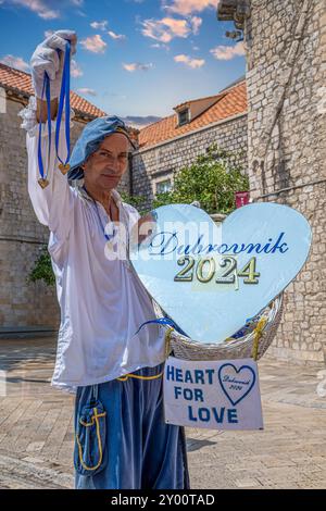 DUBROVNIK, CROAZIA - 17 AGOSTO 2024: Uomo vestito con abiti medievali, con il simbolo dell'amore, sulla strada principale della città vecchia, Stradun, di fronte Foto Stock