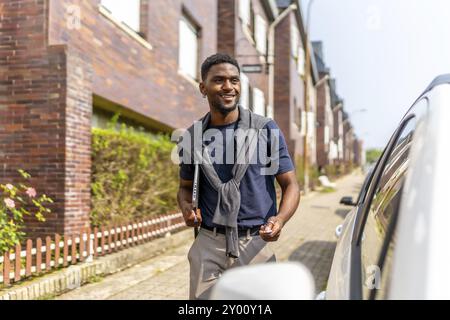 Giovane uomo d'affari africano che va a lavorare in auto aprendolo con il telecomando mentre porta un portatile in strada Foto Stock