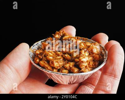 Persona in possesso di riso soffiato con torta al cioccolato in tazza di alluminio, su nero Foto Stock