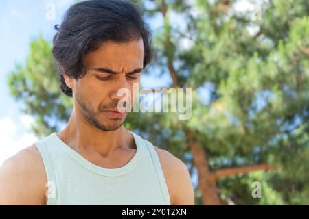 Un uomo con barba e canotta verde guarda la telecamera. Lui è profondo nel pensiero Foto Stock