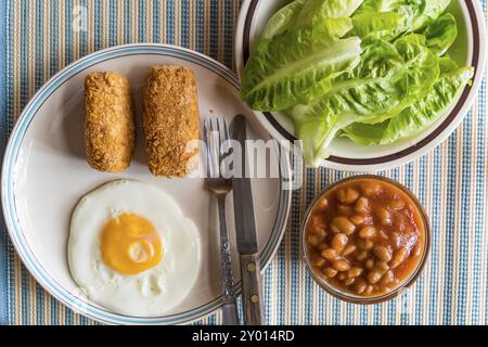 Crocchette, uova fritte, verdure fresche, fagioli bianchi in salsa di pomodoro come colazione Foto Stock