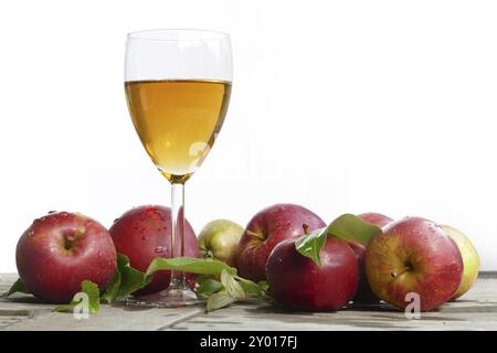 Succo di mela appena spremuto in vetro e mele rosse con foglie su legno vecchio, davanti allo sfondo bianco Foto Stock