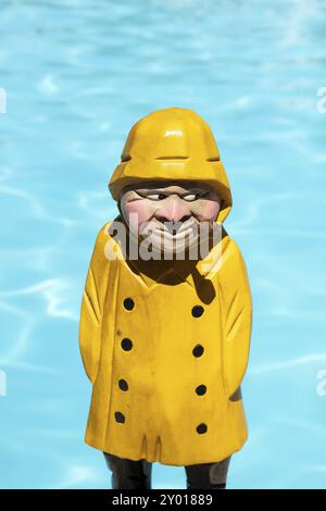 Pescatore figura in legno di colore giallo con la pioggia e il cappotto di tubo di fumo sulla piscina sullo sfondo Foto Stock