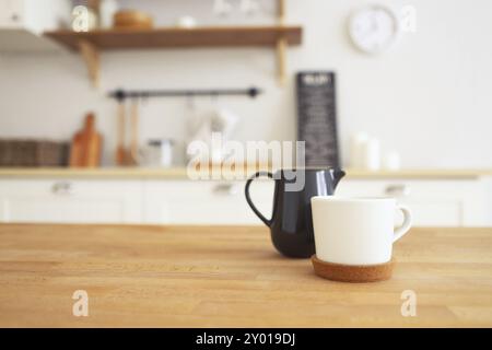 Tavolo in legno con tazza e bricco per latte con cucina sfocata sfondo, spazio di copia Foto Stock