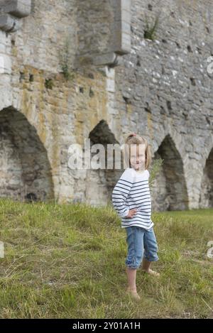 Piccola e carina ragazza che posa di fronte alle mura medievali della vecchia città anseatica di Visby sull'isola di Gotland in Svezia . Piccola e carina ragazza che sta in posa Foto Stock