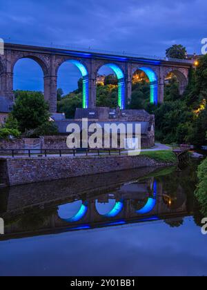 Dinan, Francia - 19 luglio 2024: Viadotto storico illuminato sopra il Port de Dinan, che si riflette nel fiume Rance, Bretagna, Francia Foto Stock