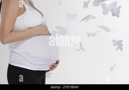 Donna incinta pancia su uno sfondo bianco con farfalla Foto Stock