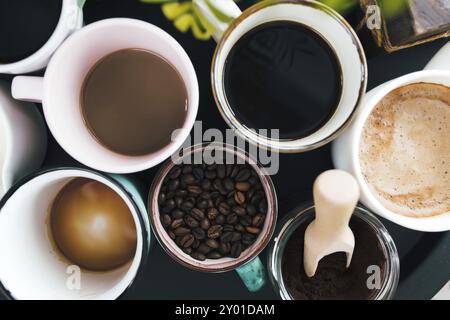 Più tazze di caffè, latte, chicchi e caffè macinato in vaso su sfondo nero. Foto Stock
