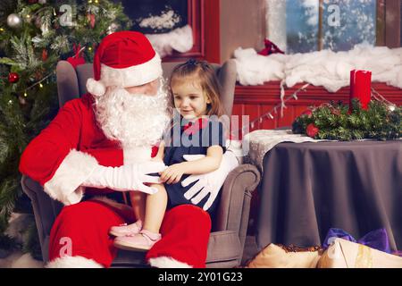 Bambina raccontando il suo augurio natalizio a Santa Claus in prossimità della struttura ad albero di Natale Foto Stock