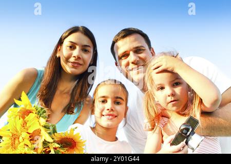 Felice famiglia di genitori e due ragazze abbracciando mentre tenendo i girasoli e sorridendo alla macchina fotografica nel campo estivo Foto Stock