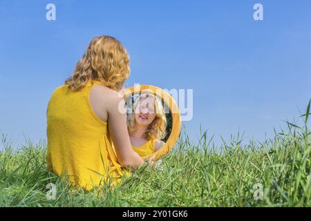 I capelli rossi donna siede guardando la sua immagine speculare al di fuori Foto Stock