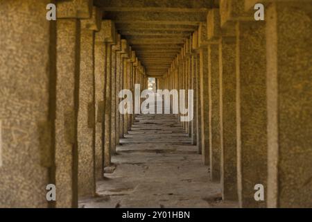 Le colonne di pietra si ripetono lungo un lungo passaggio coperto nelle antiche rovine di Hampi, Karnataka, India, Asia Foto Stock